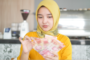 ibu rumah tangga memegang uang rupiah hasil usaha sampingan ibu rumah tangga